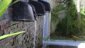 A water feature with multiple spouts against a brick wall, surrounded by rocks and plants. - Residence Argine Apartments (Mahé Island)
