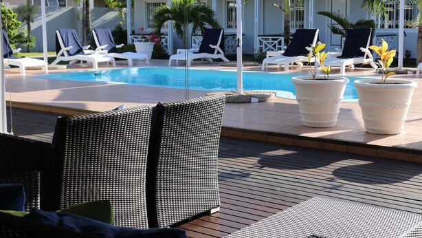 A poolside area with lounge chairs, umbrellas, and potted plants. - Residence Argine Apartments (Mahé Island)