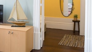 A hallway with a wooden cabinet, a sailboat model, a framed picture, a mirror, and a small table with a plant. - Merc Porto Central (Porto)