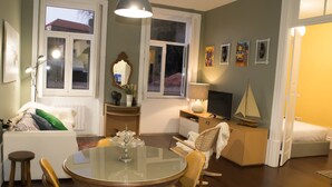 A cozy living room with a round glass table, wooden chairs, a sofa, and a television. - Merc Porto Central (Porto)