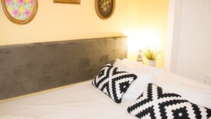 A bed with a grey headboard, white bedding, and black and white patterned pillows. There are two framed artworks on the wall above the bed. - Merc Porto Central (Porto)