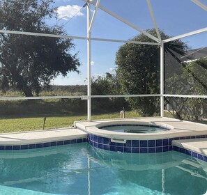 A swimming pool with a blue tiled edge, surrounded by a white fence, and a clear view of trees and sky.