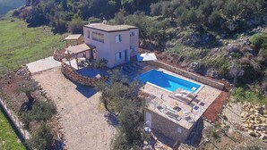 A modern two-story house with a swimming pool, surrounded by a stone wall and a garden.