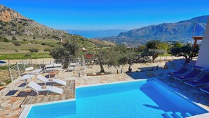 A swimming pool with lounge chairs, a stone deck, and a view of a mountainous landscape.