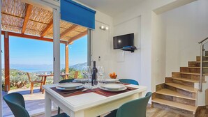 A dining area with a table set for two, a TV mounted on the wall, and a staircase leading to an upper level.