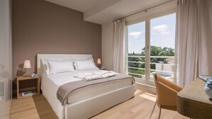 Un dormitorio con una cama grande, mesitas de noche, una silla y vistas al verdor a través de la ventana.