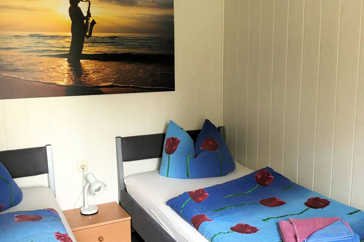 Un dormitorio con dos camas, una mesita de noche, una lámpara y un cuadro de una persona tocando el saxofón en la playa al atardecer.