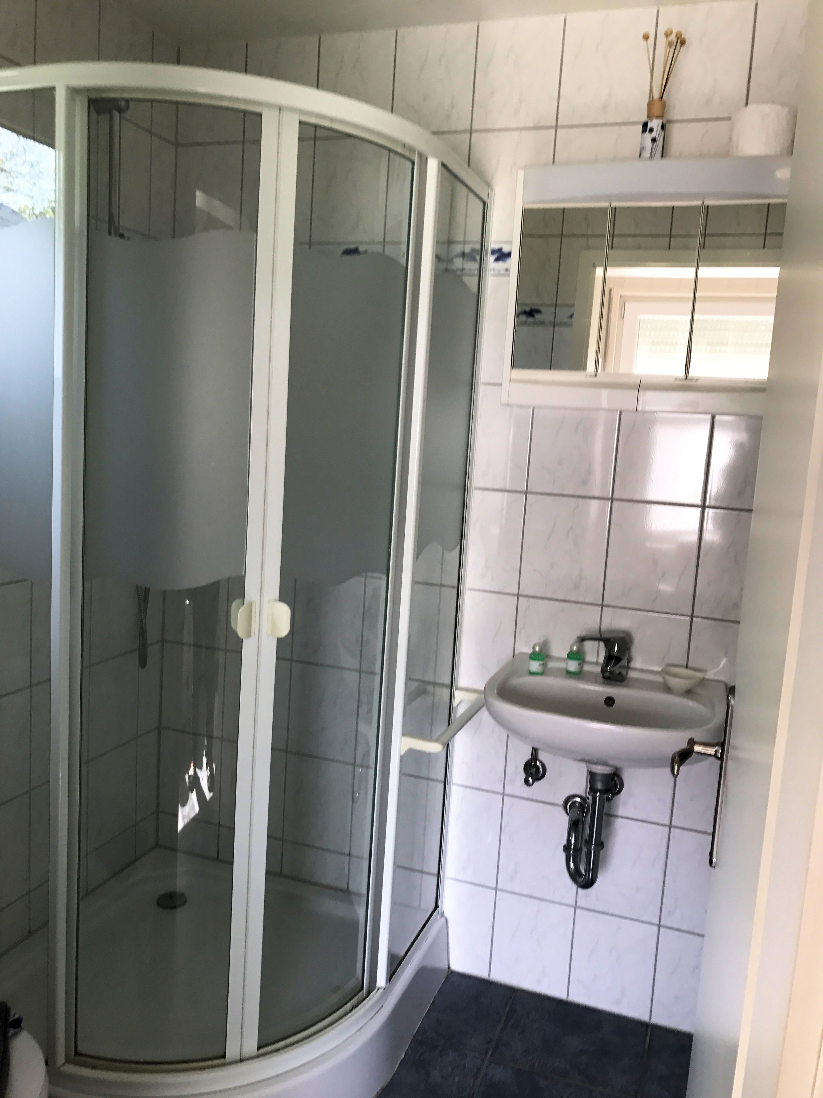 A bathroom with a glass-enclosed shower, a sink with a mirror above it, and tiled walls.