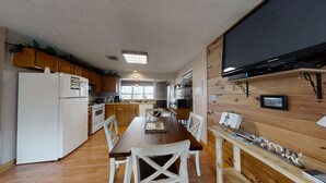 A kitchen with wooden cabinets, a white refrigerator, a wooden dining table with chairs, and a mounted flat-screen TV.