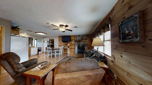 A cozy cabin interior with a stone fireplace, wooden walls, a dining area, and a television.