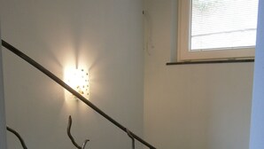 Un escalier avec une rampe en métal en forme de branche, un luminaire fixé au mur et une petite table sur laquelle est posé un train jouet.