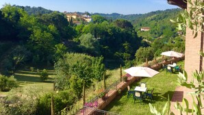 Une terrasse avec une table et des chaises, entourée d’une végétation luxuriante et offrant une vue sur une colline parsemée de bâtiments.