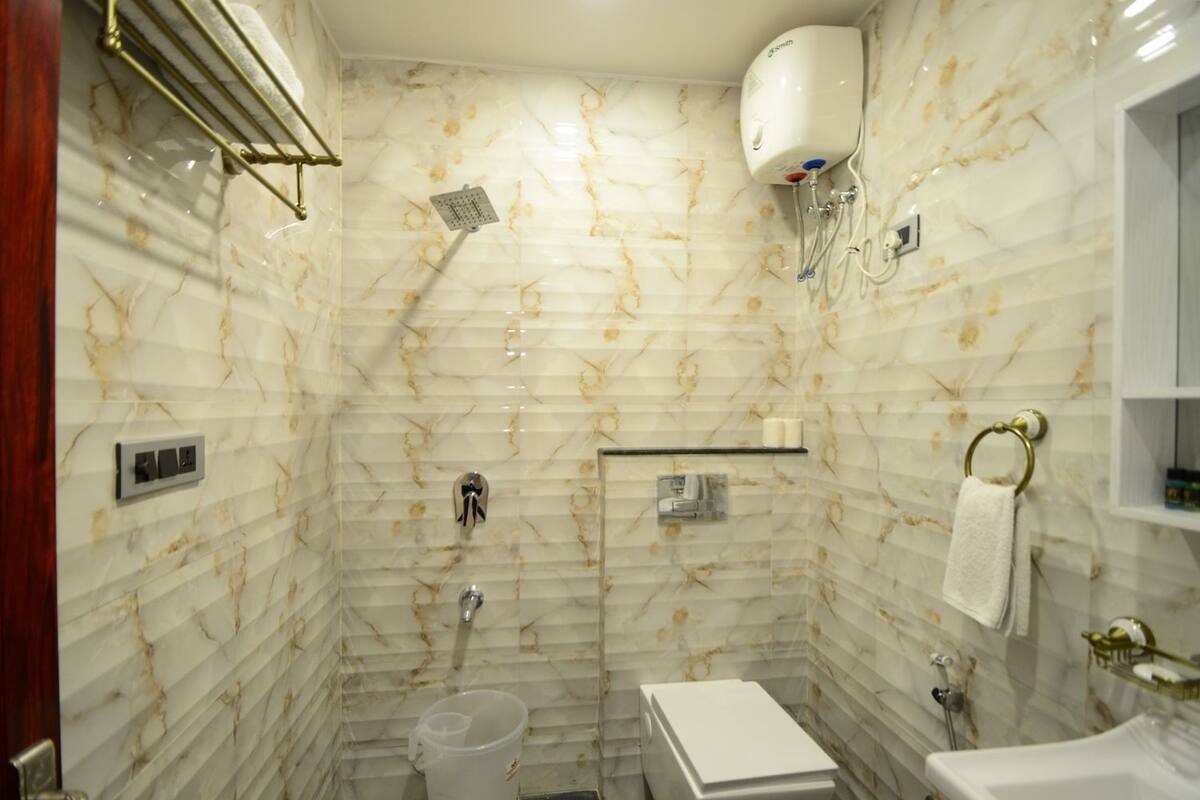 A bathroom with a marble wall, a shower, a toilet, and a sink.
