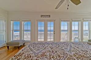 Quarto com uma cama grande, um banco e vista para a praia através de várias portas.