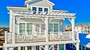 Una casa de dos pisos con balcón, pérgola y vista a la playa.