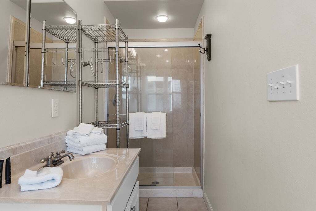 A modern bathroom with a glass-enclosed shower, a sink with a mirror, and a towel rack.