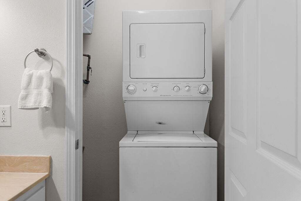 A compact laundry room with a front-loading washer and dryer, a towel rack, and a wooden countertop.