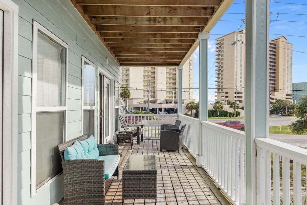 A covered porch with wicker furniture, a glass table, and a view of tall buildings in the background.
