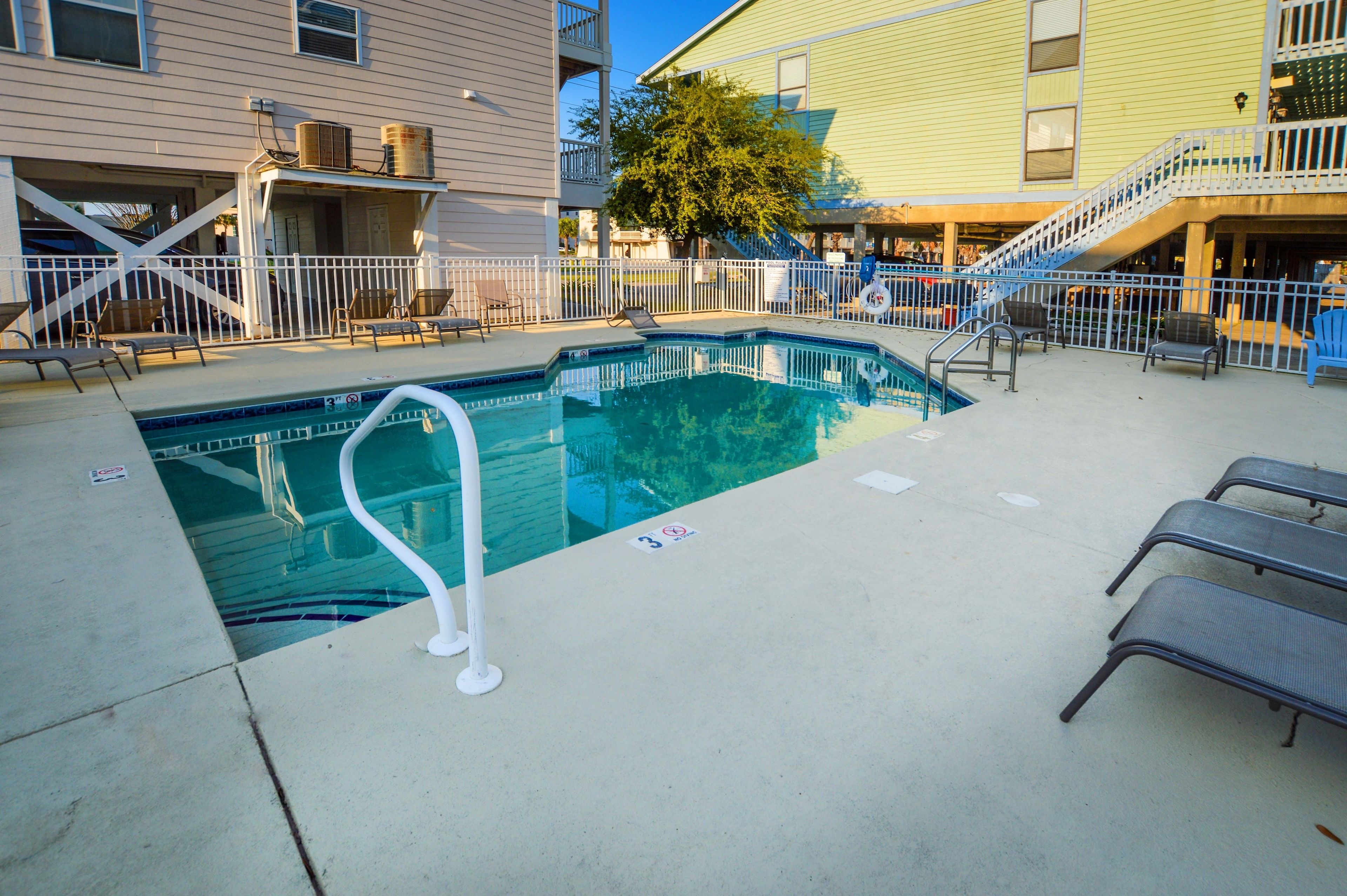 A swimming pool with a white fence, lounge chairs, and a staircase leading to an upper level.
