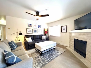 A living room with a sofa, a coffee table, a fireplace, and a ceiling fan.