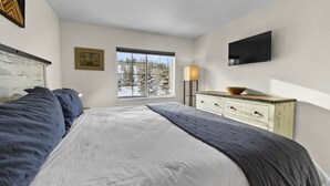 Une chambre avec un grand lit, une commode, une télévision et une fenêtre donnant sur des arbres.