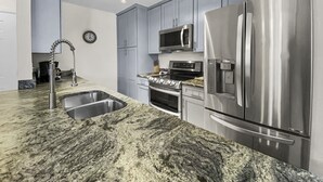 Une cuisine moderne dotée de plans de travail en granit, d’appareils électroménagers en acier inoxydable et d’armoires de couleur gris clair.