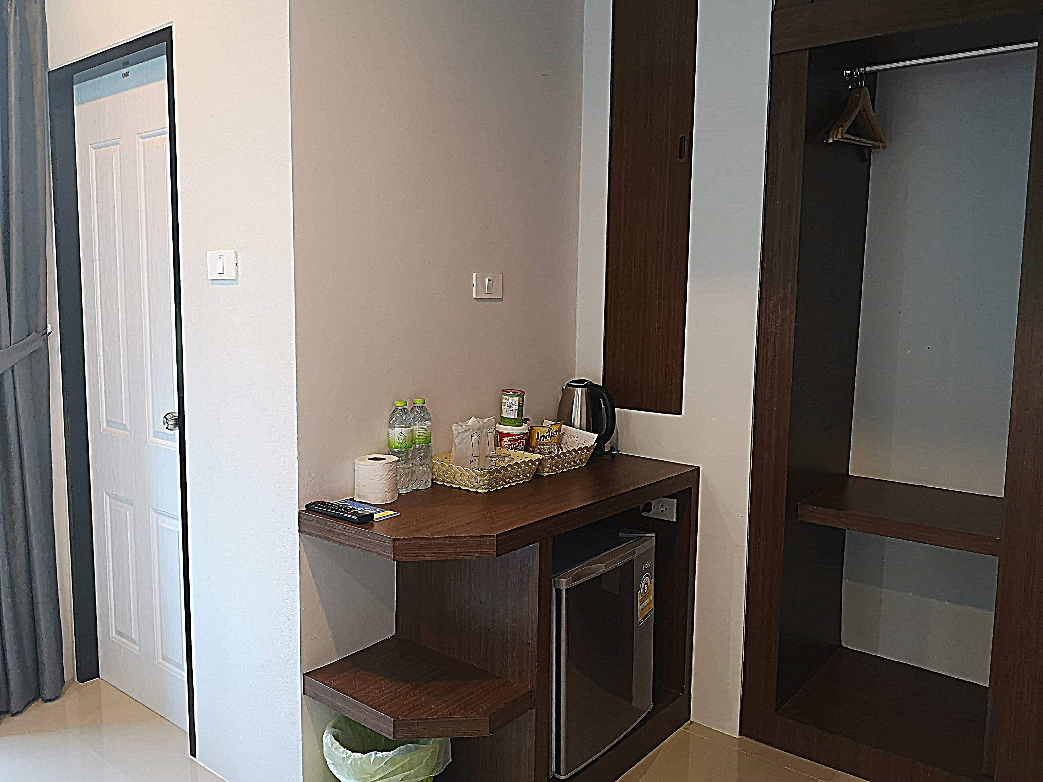 Una habitación compacta con escritorio de madera, un refrigerador pequeño y un cesto de basura.