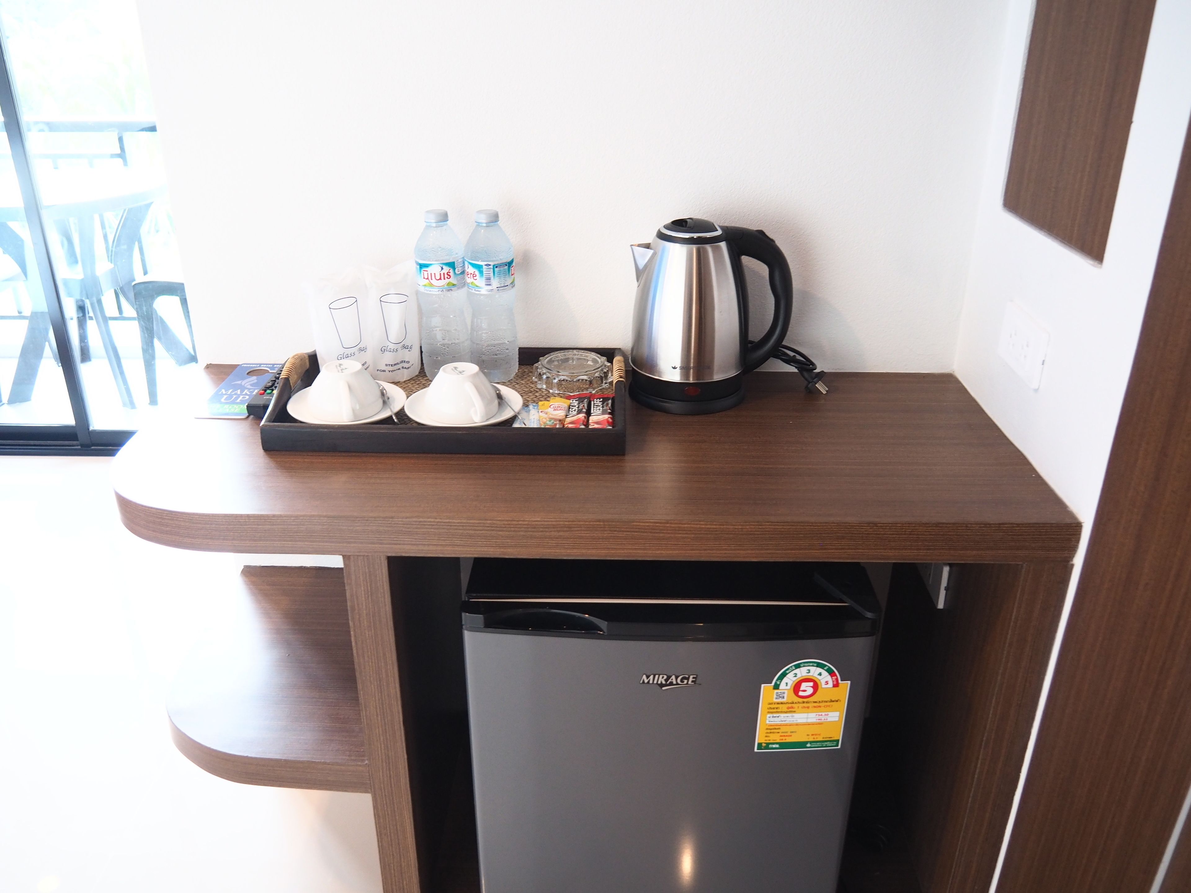Een kleine keuken met een koelkast, een koffiezetapparaat en een dienblad met glazen en flessenwater.