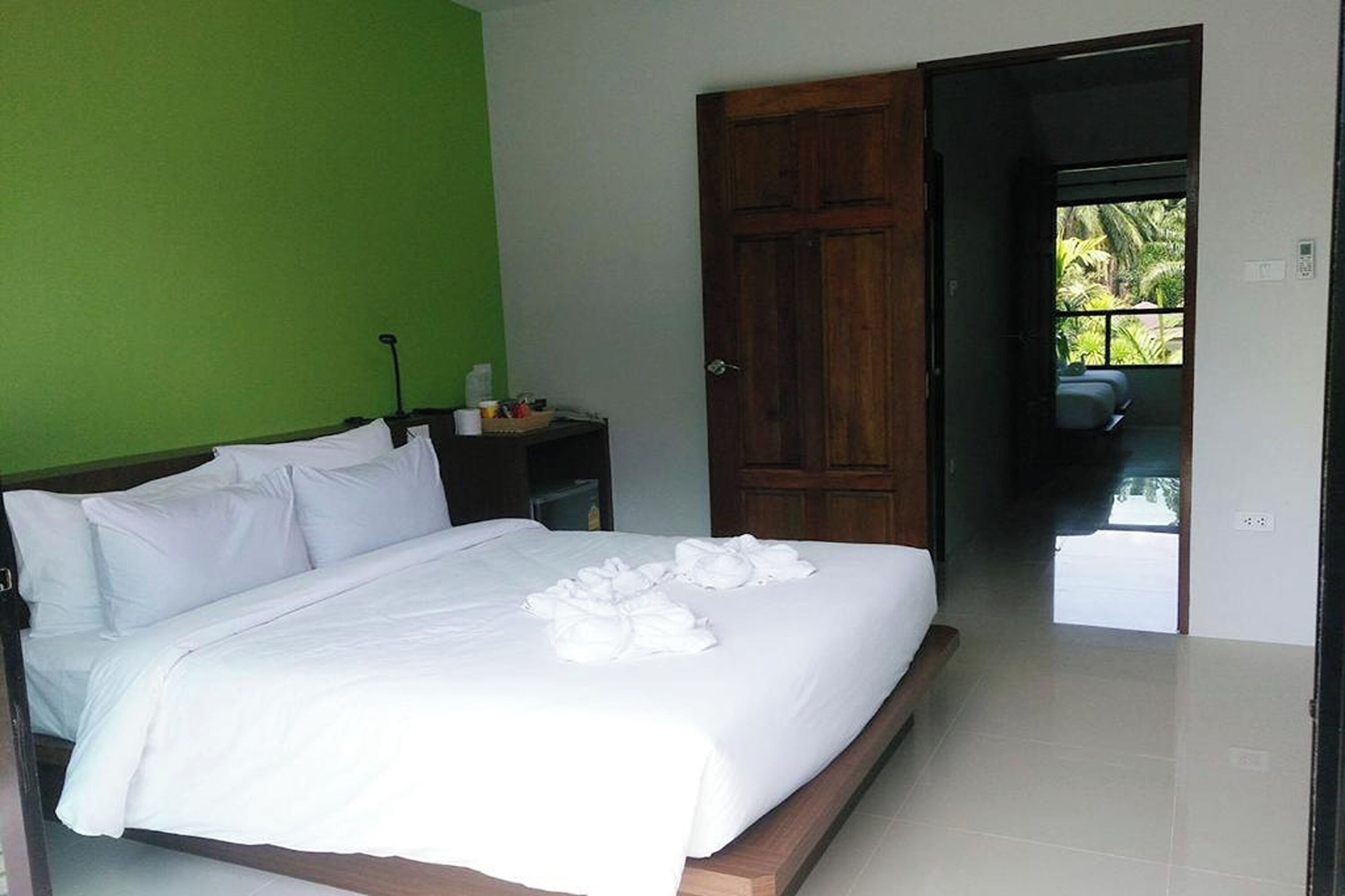 A neatly made bed with white linens and towels, a wooden nightstand with toiletries, and a green wall.