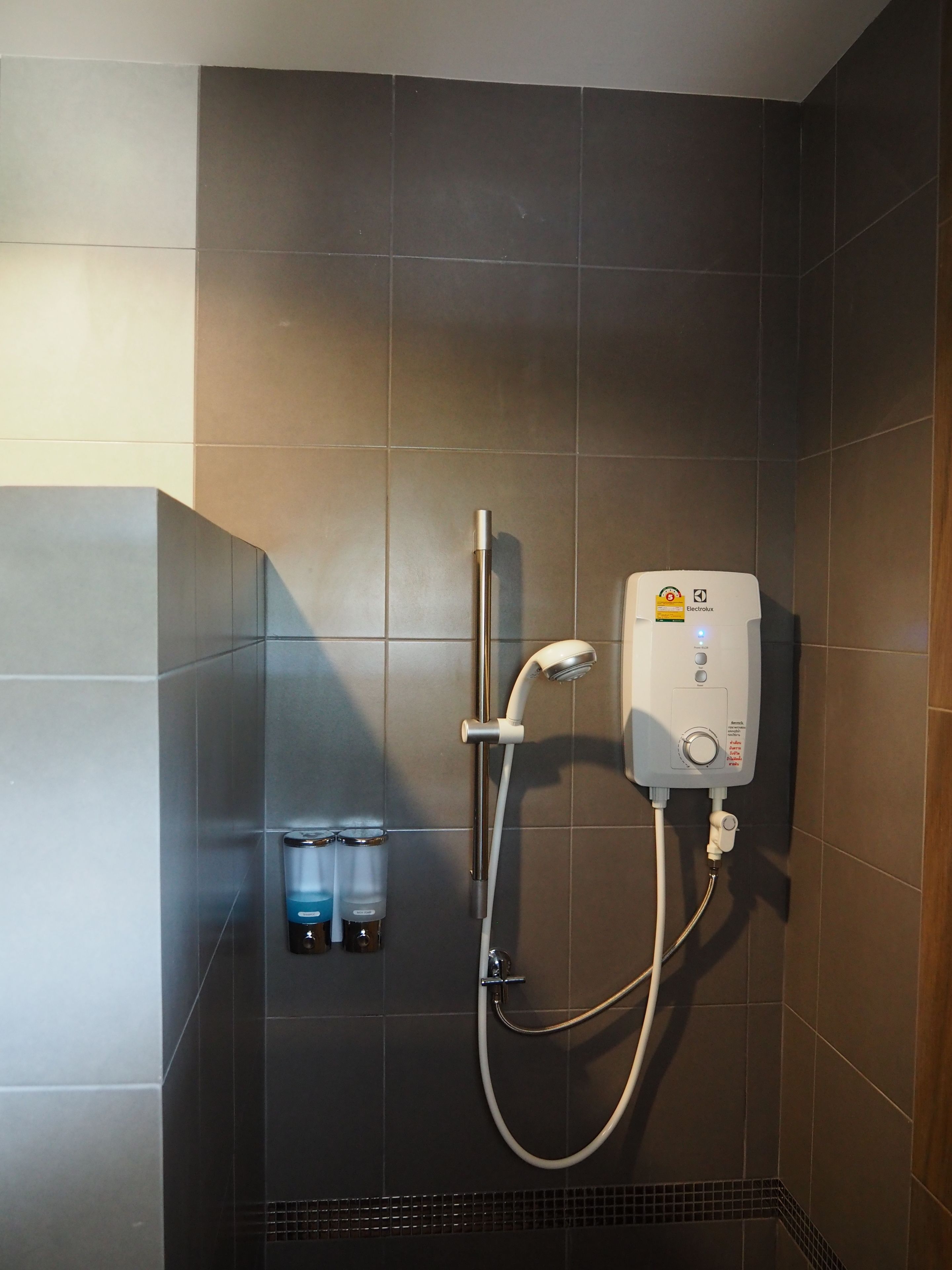Un área de ducha con cabezal de ducha y control de pared, un perchero y dos dispensadores de jabón.