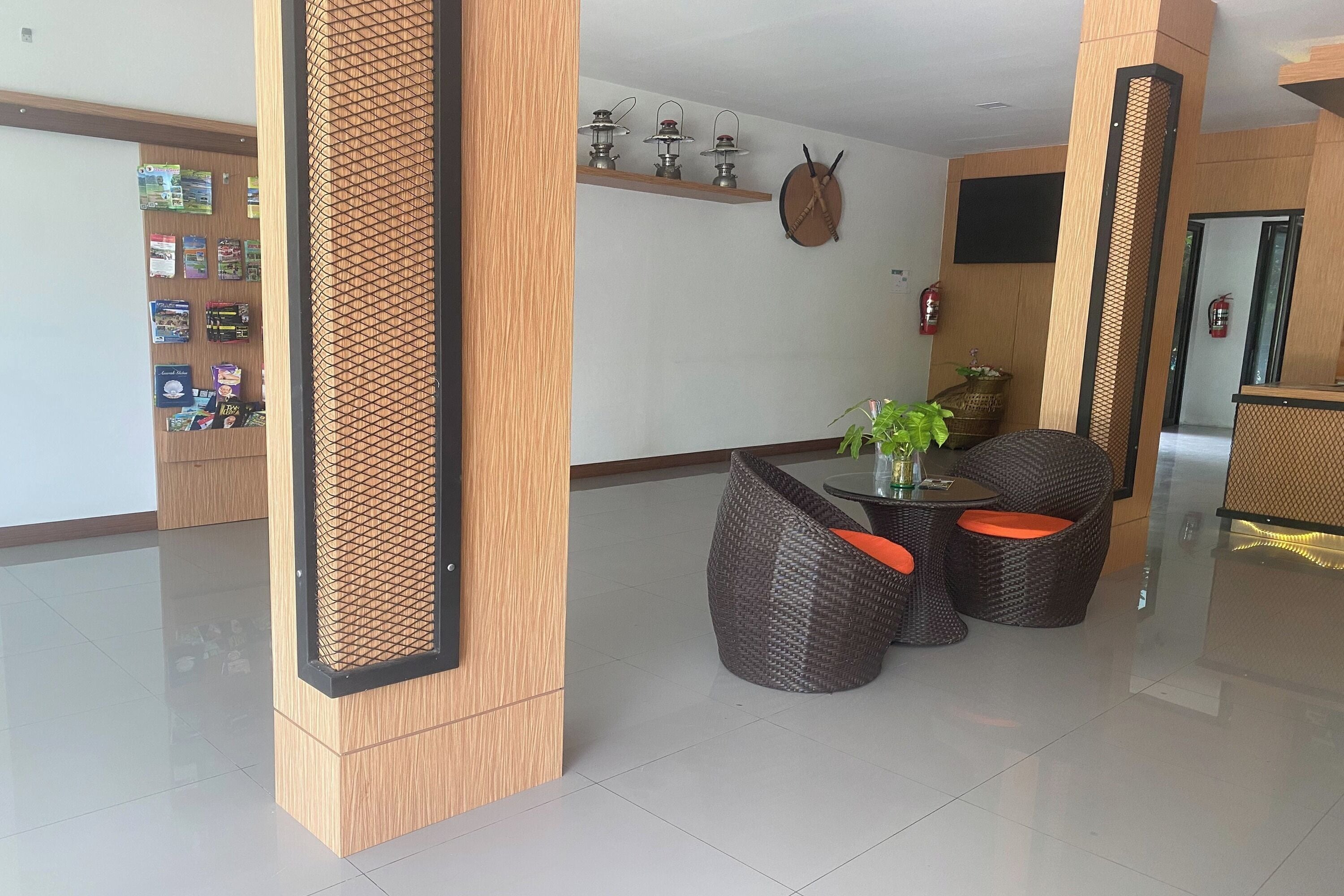 A lobby with a reception desk, wicker furniture, a wall-mounted shelf with decorative items, and a bulletin board with pamphlets.