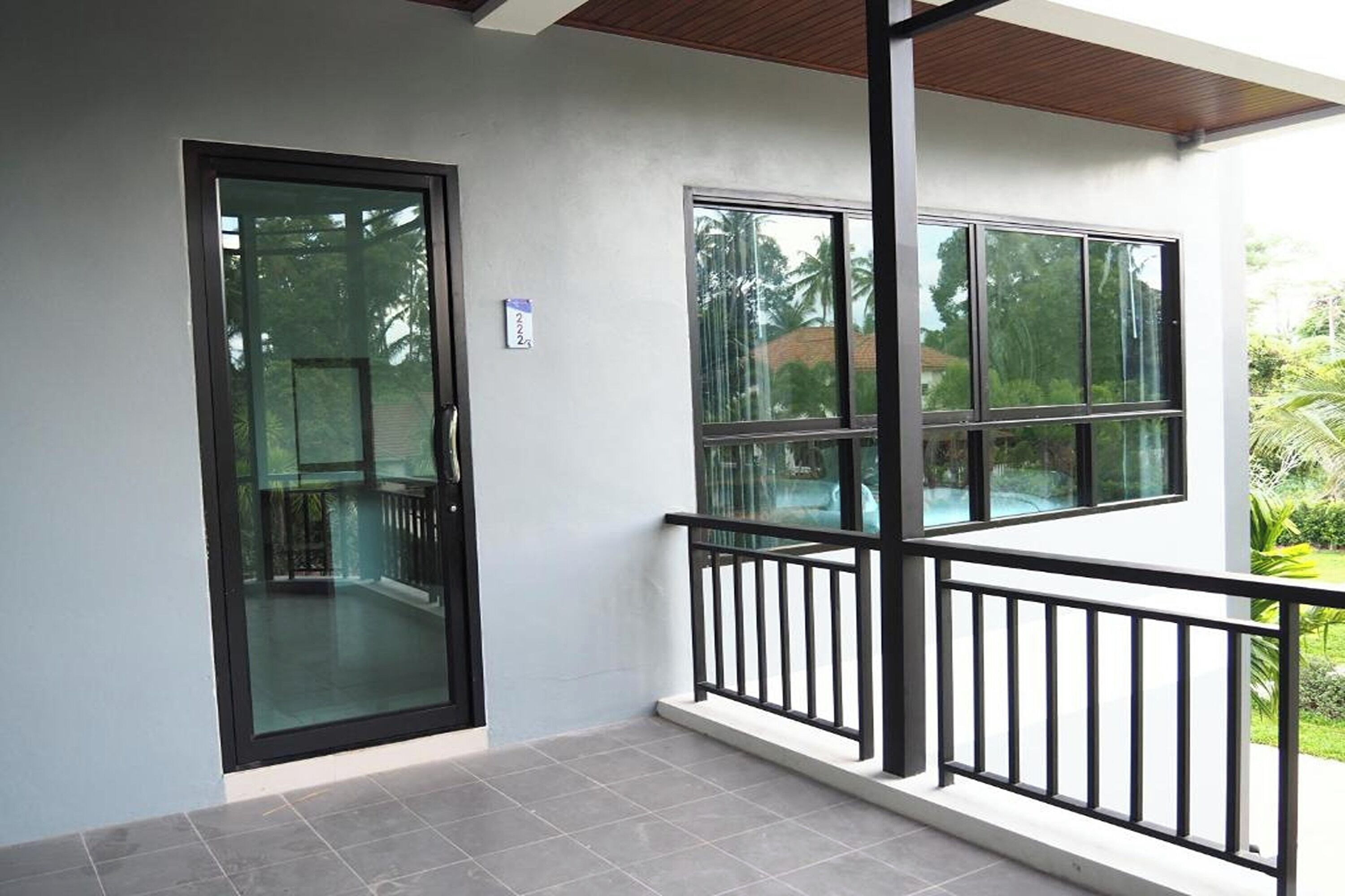 A modern building with a glass door and windows, a balcony with a black railing, and a tiled floor.