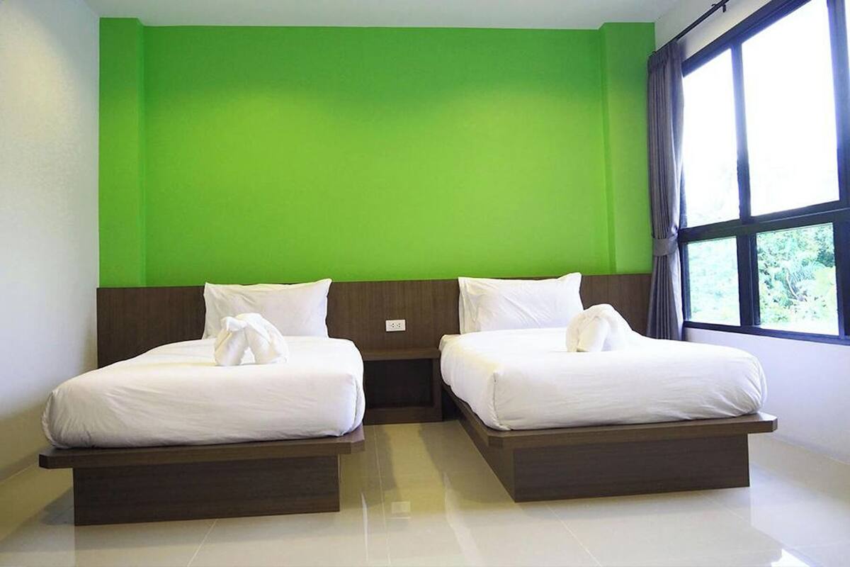 A hotel room with two beds, a green wall, and a window with curtains.
