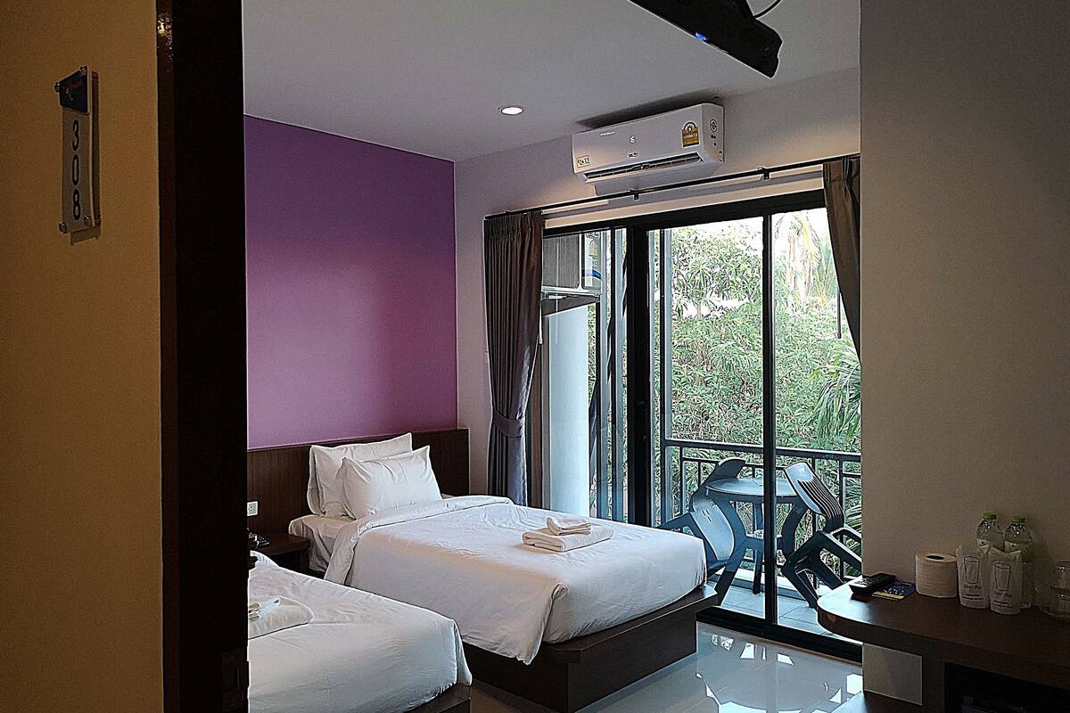 A hotel room with two beds, a balcony with a table and chairs, and an air conditioning unit.