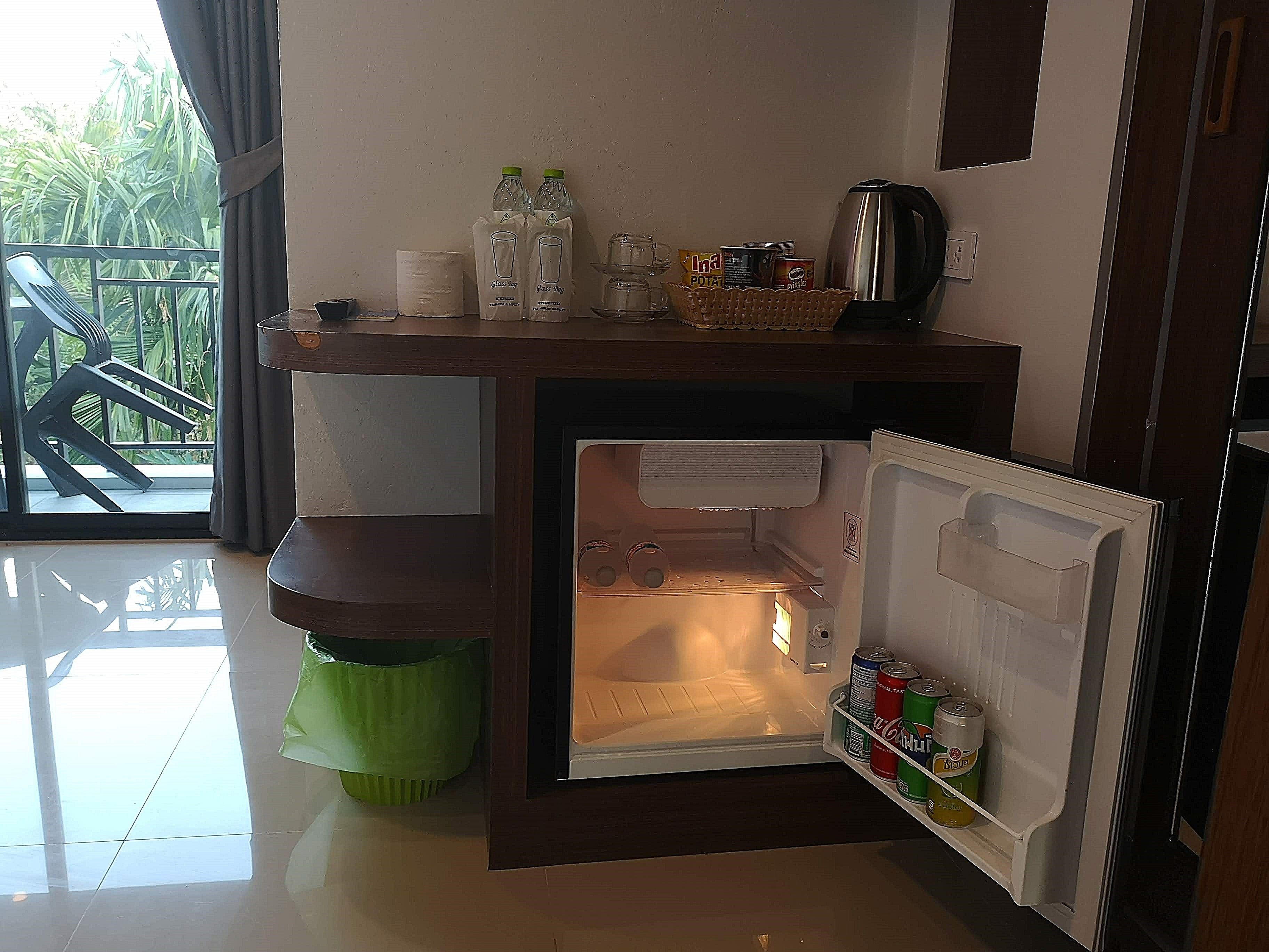 Een kleine keuken met een koelkast, een koffiezetapparaat en een klein wastafeltje.