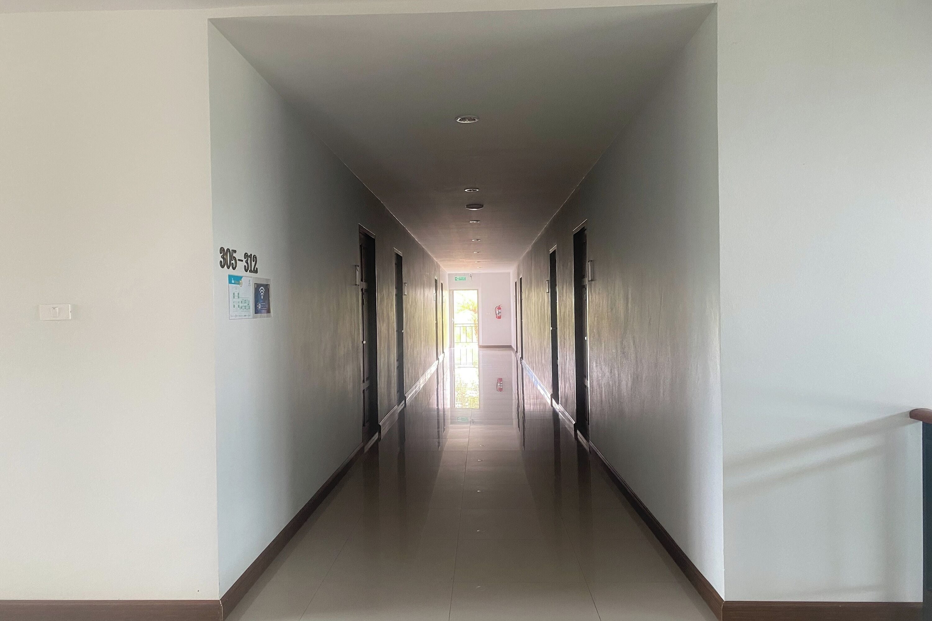 A long, narrow hallway with a series of doors on both sides, leading to a bright exit at the end.