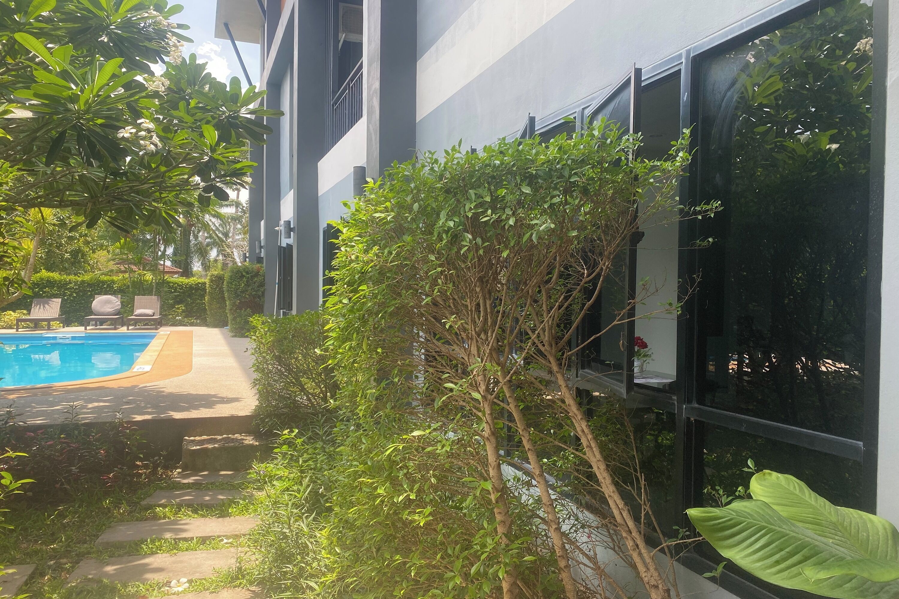A modern building with a swimming pool, surrounded by lush greenery and a clear sky.