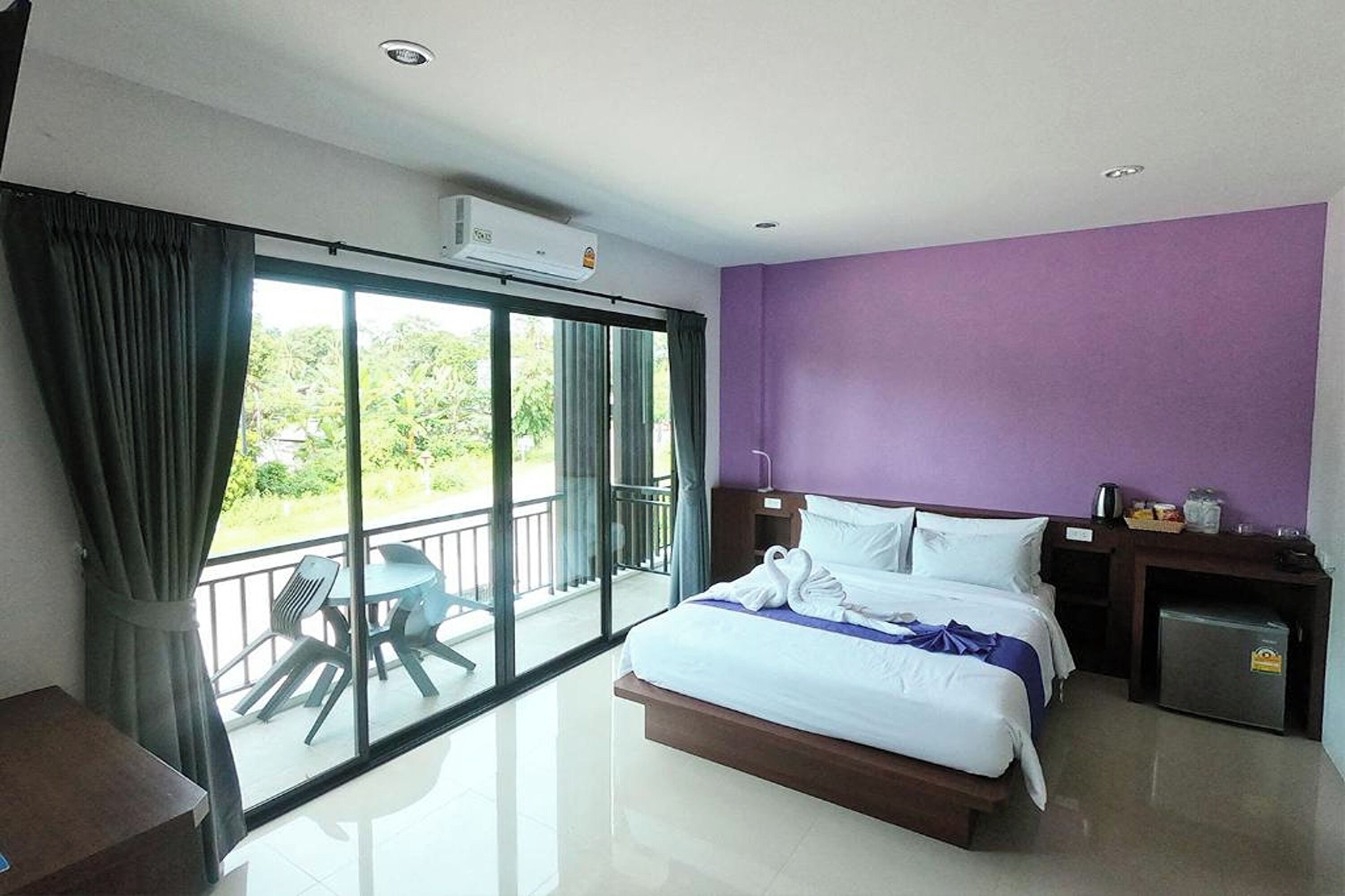 Habitación de hotel con cama, escritorio, silla y balcón con vistas a zonas verdes.