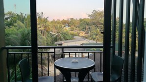 Varanda com mesa redonda e duas cadeiras, com vista para uma área residencial com casas e vegetação.
