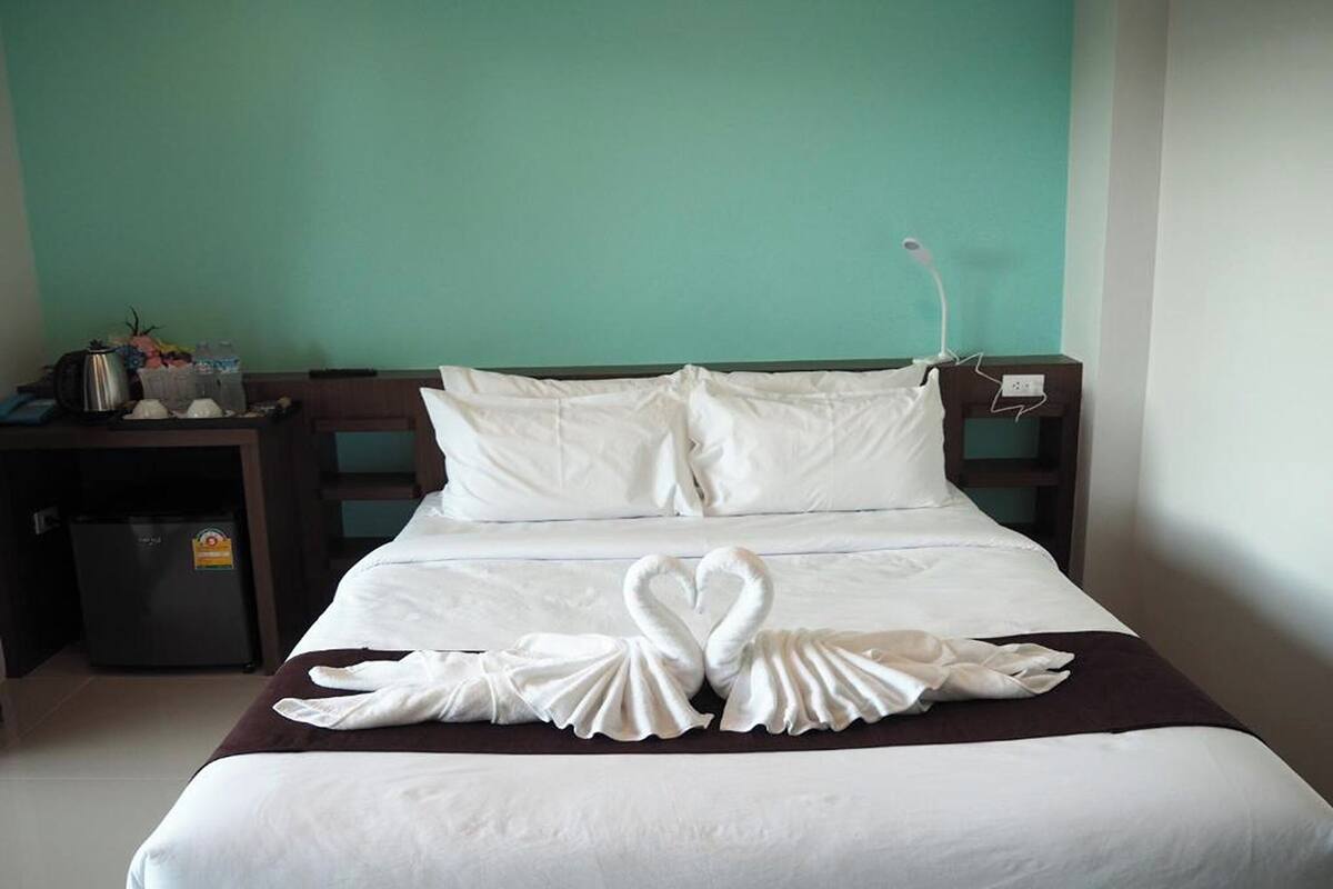 A hotel room with a bed, two pillows, a nightstand with a lamp, a small fridge, and a wall-mounted phone.
