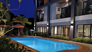 A swimming pool with a curved edge, surrounded by a landscaped area with plants and a seating area with umbrellas. - Friendly Hotel Krabi (Krabi)