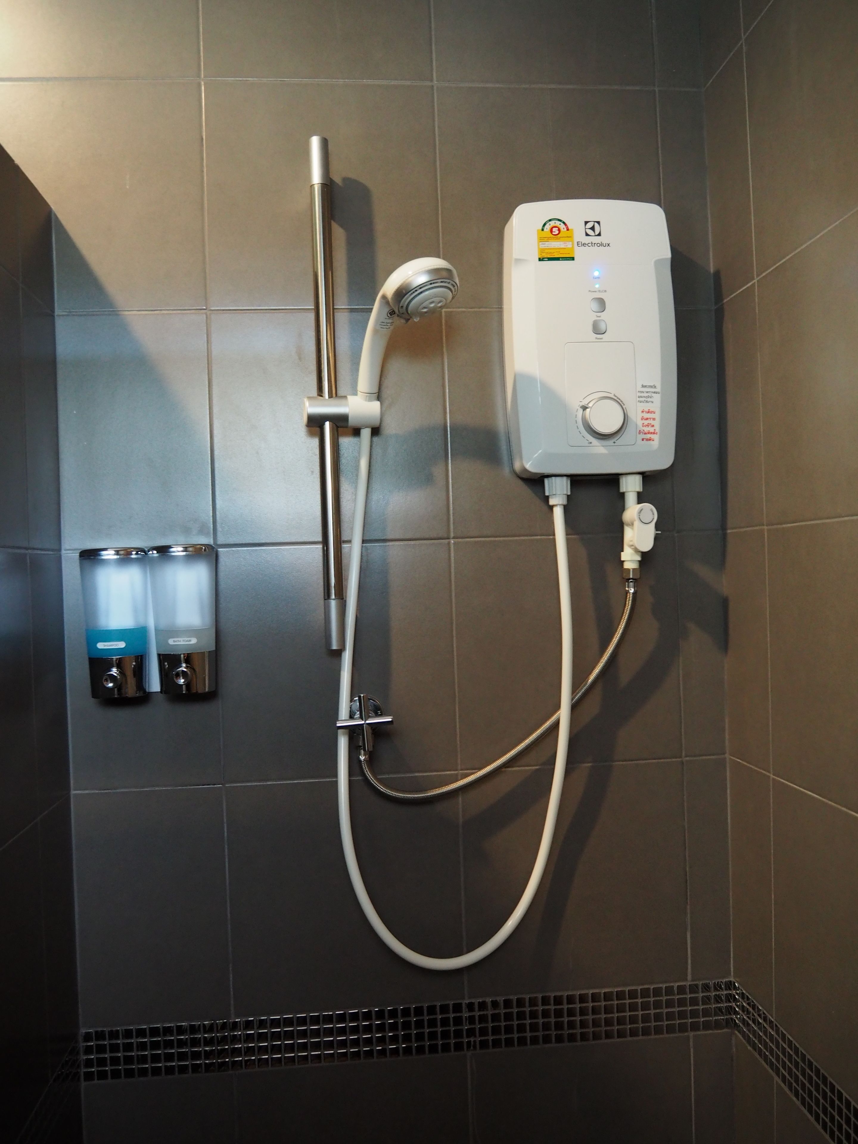 A wall-mounted shower unit with a control panel, a handheld showerhead, and two soap dispensers.