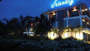 Um edifício moderno com uma placa 'Friendly', cercado por palmeiras e caminhos bem iluminados.