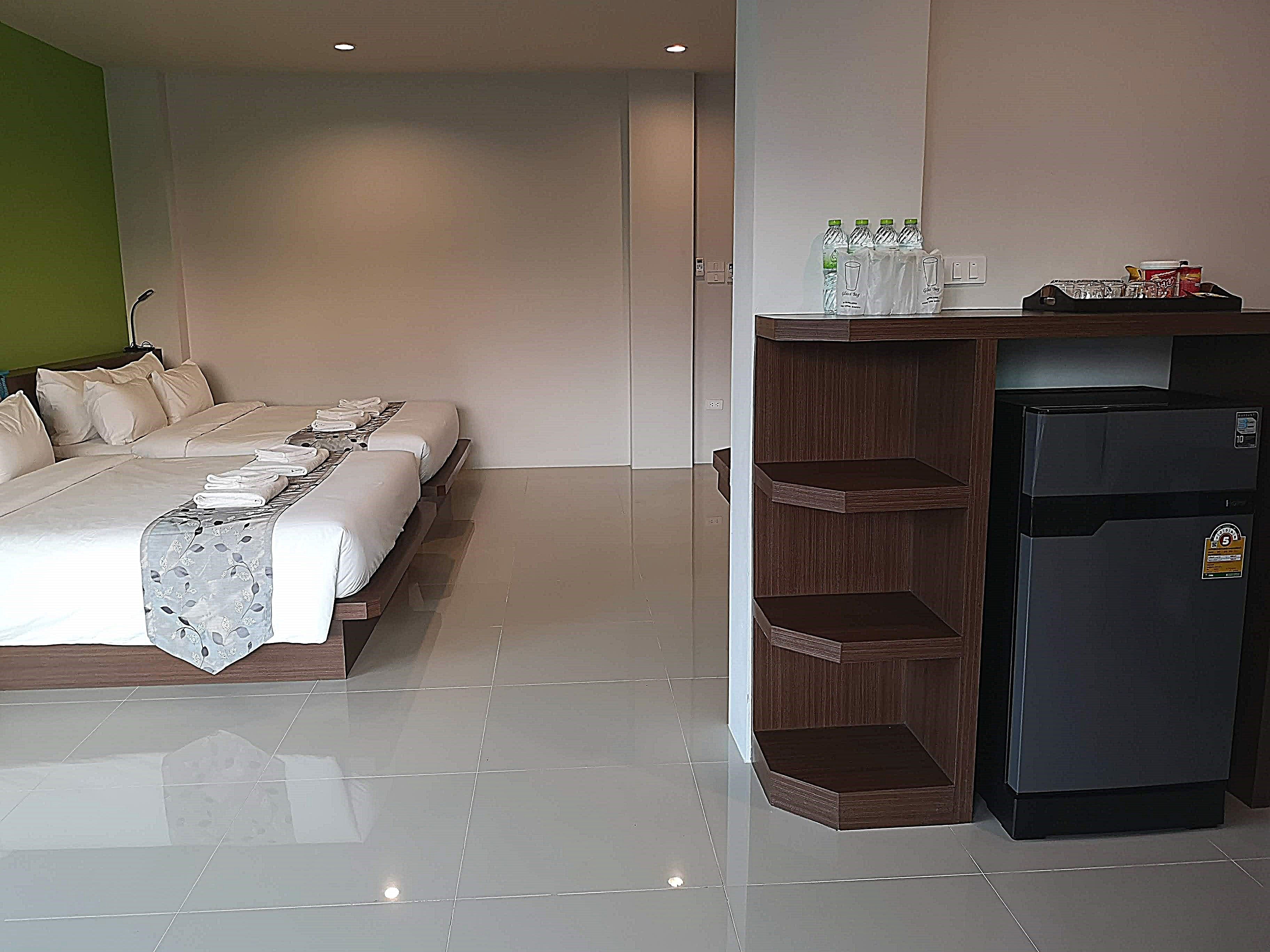 Ein Hotelzimmer mit einem großen Bett, einem Holztisch mit einem Kühlschrank und einem Regal mit Wasserflaschen.
