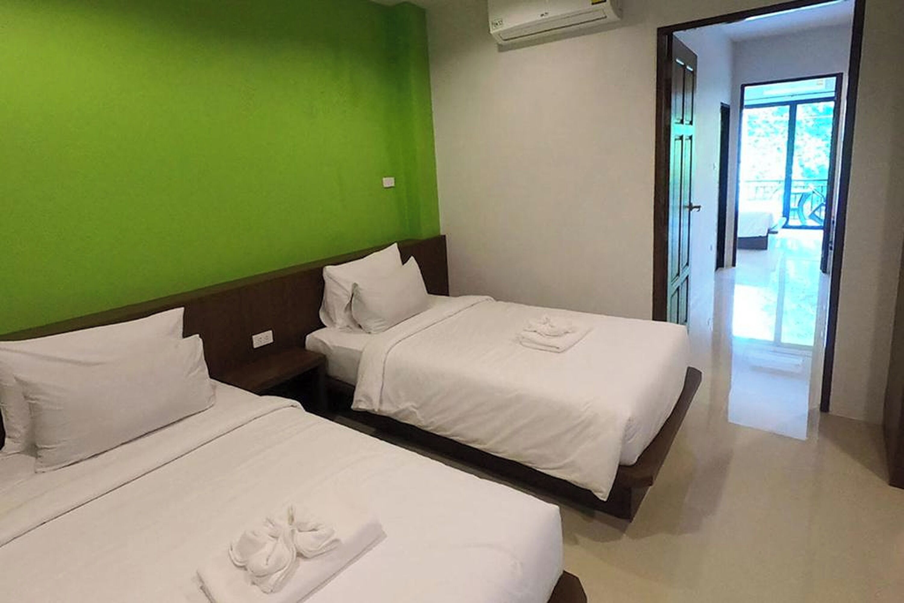 A hotel room with two beds, a green wall, and a view of the outside.