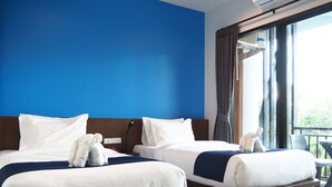 Quarto de hotel com duas camas, uma parede azul de destaque, uma janela grande com cortinas e uma varanda.