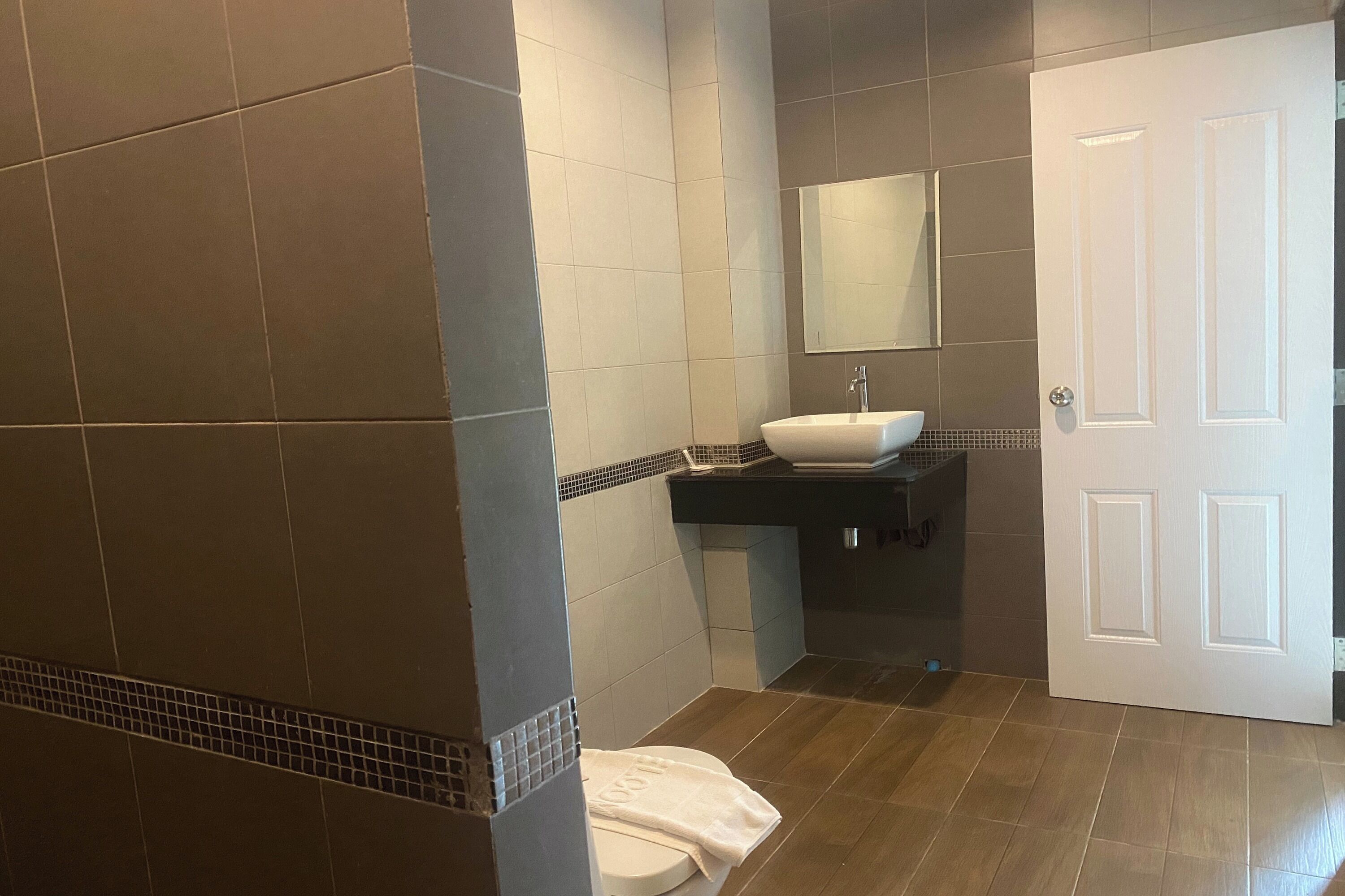 A bathroom with a white toilet, a sink with a mirror above it, and a door.