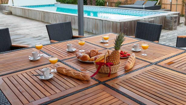 Eine Holzterrasse mit Poolbillard, Stühlen und Frühstücksangeboten, darunter Croissants, Brot und Obst.