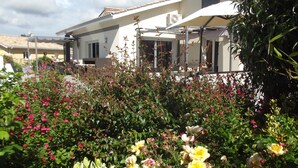 Ein Wohngebäude mit überdachter Terrasse, umgeben von üppigem Grün und blühenden Pflanzen.