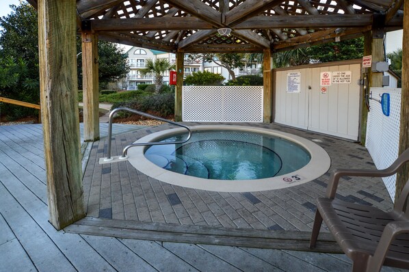 A hot tub under a wooden pergola with a white fence and signs indicating no swimming under 12 and no hot tub use.